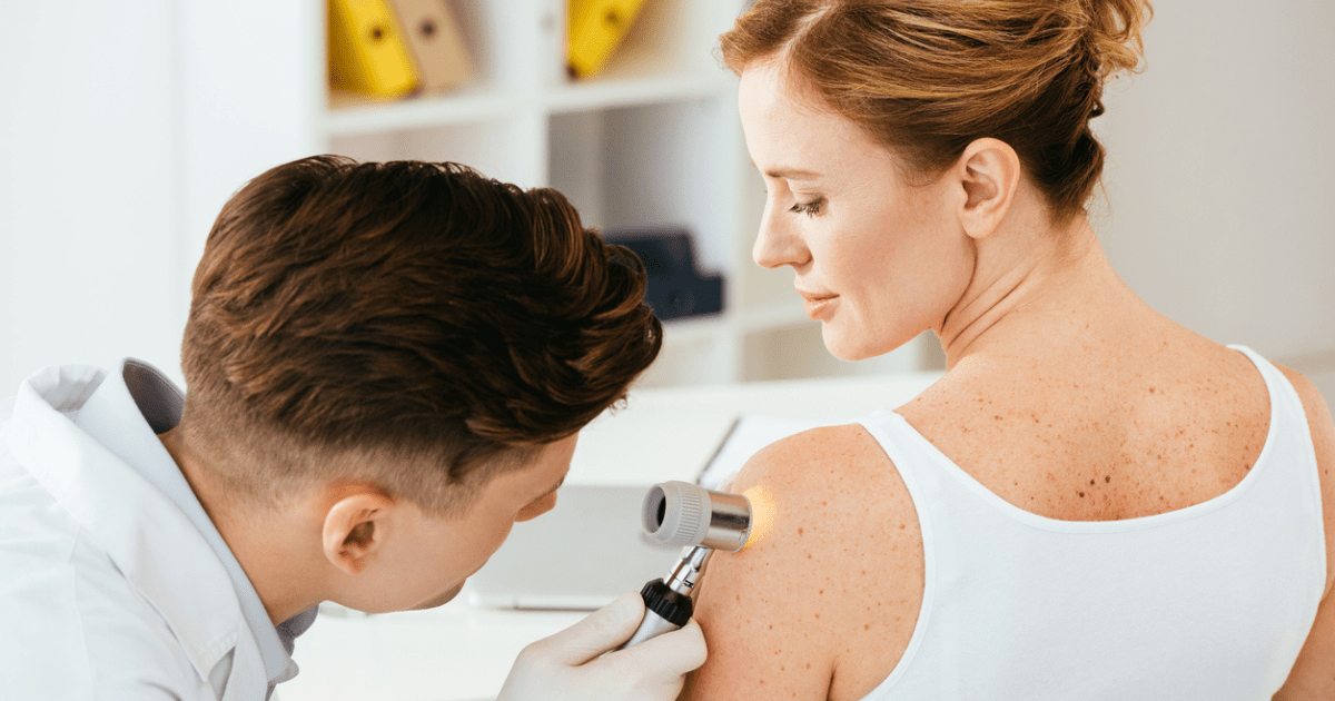 A medical dermatologist examining the skin of a female patient's arm.
